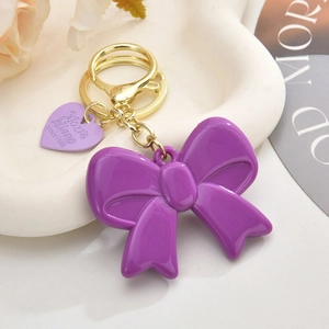 Chic purple acrylic bow keychain with gold metal ring on a minimalist white tray