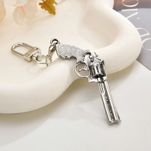 Detail of vintage silver revolver keychain with textured grip on a white ceramic tray