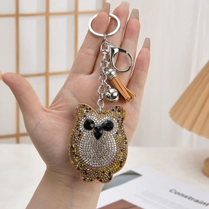 Close-up of owl rhinestone keychain with leather tassel and decorative bell on a bag
