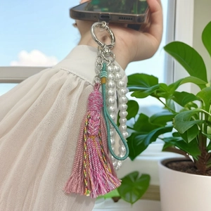 Bijou de téléphone fait main avec pompons mauves, perles blanches et cordon tressé vert
