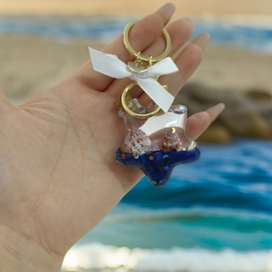 Detail eines sternförmigen Flaschenanhängers mit blauem Sand und Ozean-Glitzersteinen