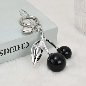 Detailed view of glossy black cherry keychain with silver leaves and heart charm on plush