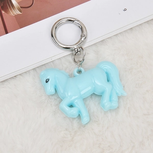 Detail of light blue acrylic horse keychain with silver metal hook on white faux fur