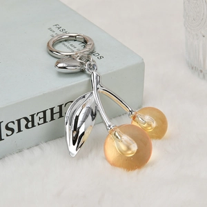 Creative silver cherry keychain pendant with amber resin fruit on a white plush surface
