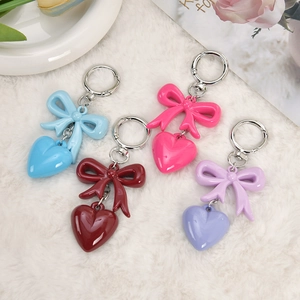 Sweet heart and bow keychain charms in rose red, blue, and purple displayed on plush white rug