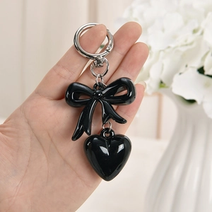 Glossy black bow with heart pendant keychain and silver ring shown in hand