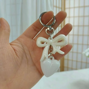 Close-up of a white resin bow and heart-shaped pendant keychain held in hand