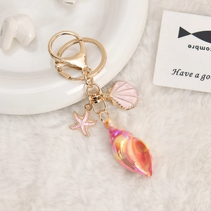 Detail view of gold keychain with starfish and shell pendants on soft white fabric