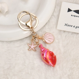Detail of a pink seashell and starfish keychain on a white plush background