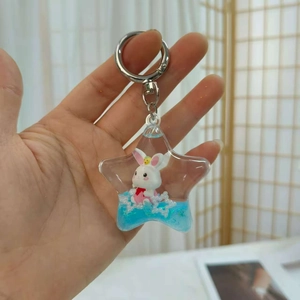 Close-up of star-shaped keychain with white rabbit in blue liquid sand