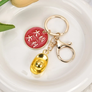 Golden keychain with Good Luck pendant and gold ingot charm on white ceramic tray