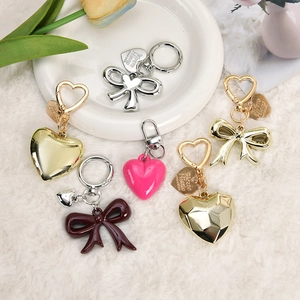 Detail of red bow and heart pendants on a metal keychain displayed on white plush fabric