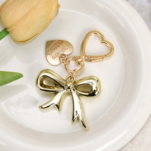 Close-up of a gold bow keychain with heart clasp and heart charm on a ceramic tray