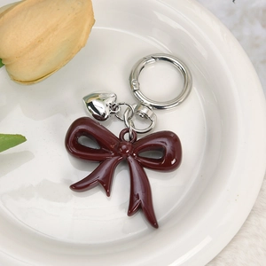 Close-up of deep red resin bow keychain with silver heart mirror charm on white plate