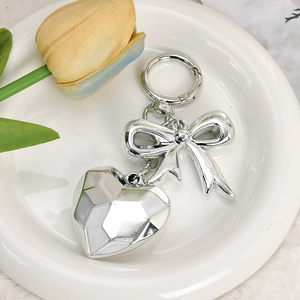 Close-up of silver bow and faceted heart charm keychain on a white ceramic plate