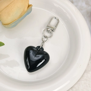 Close-up of a glossy black heart charm with a silver lobster clasp on a white plate