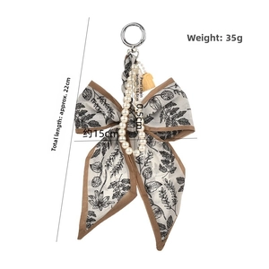 Détail du charm de sac nœud en soie avec chaîne de perles et motif floral beige