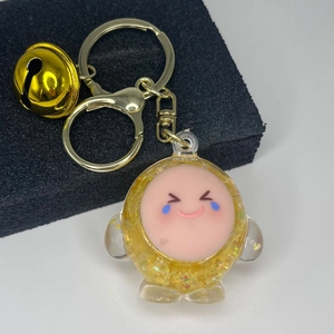 Detail of yellow glitter liquid keychain with cute crying-laughing emoji and metal bell