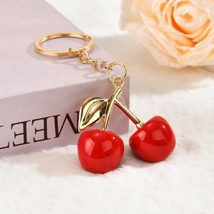 Close-up of a red cherry keychain with gold leaves on a white faux fur surface