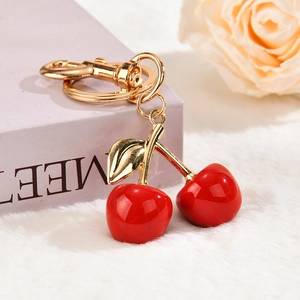 Detailed close-up of red cherry charms with gold hardware on a soft pastel background