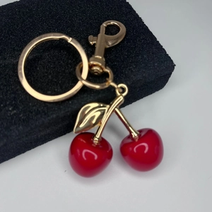 Macro view of a red cherry keychain pendant with golden metal leaves and lobster clasp