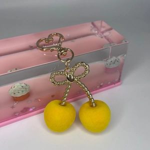 Close-up of yellow flocked cherry pendant with golden bow and heart-shaped lobster clasp