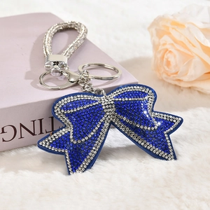 Sparkling dark blue rhinestone bow keychain with silver hand strap on white plush surface