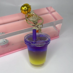 Close-up of creative liquid sand milk tea cup keychain with purple gradient and gold bell