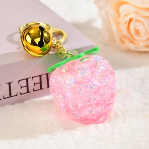 Pink strawberry keychain with glitter filling and golden bell on a white plush background