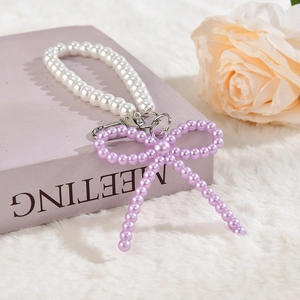 Détail d'un porte-clés perlé avec nœud violet et perles blanches sur un livre