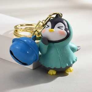 Niedlicher Pinguin-Schlüsselanhänger im türkisen Regenmantel mit großer blauer Glocke