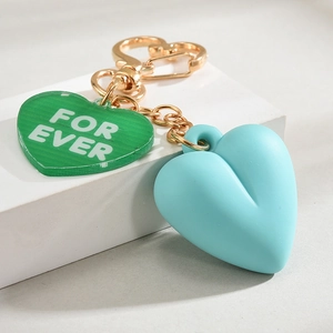 Detail of heart-shaped keychain with green acrylic tag and blue 3D silicone heart charm