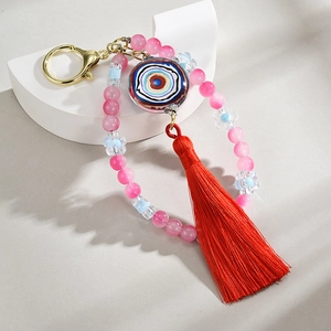 Macro detail of handmade evil eye keychain with pink beads and bright red silk tassel charm