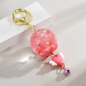 Porte-clés pailleté rose avec breloque cœur et mini cloche sur fond minimaliste blanc