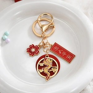 Close-up of golden dragon keychain with red floral charm and safety blessing tag