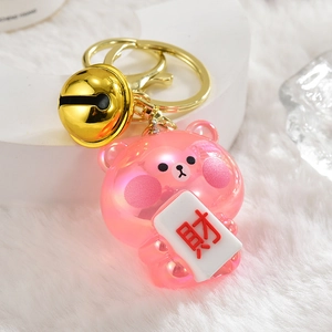 Pink translucent bear keychain with gold bell and lucky charm on plush white background