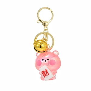 Pink jelly bear keychain with gold bell and mahjong fortune tag on white background