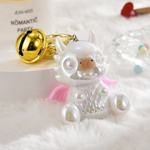 Detail of cute pearlescent white dragon mascot keychain with a large golden bell
