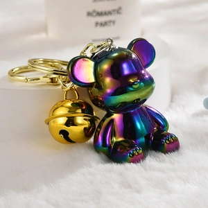 Close-up of iridescent gradient bear keychain with golden bell on plush background