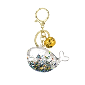 Luminous whale keychain with star sequins and golden bell charm on white background