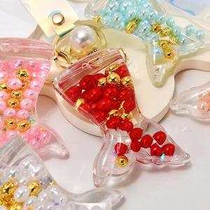 Detail of mermaid tail keychains with colorful pearls and liquid sand in acrylic shell
