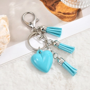 Detail of light blue heart keychain with soft tassels on a white plush surface