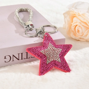 Macro detail of star keychain with pink rhinestones and silver tassel on plush background