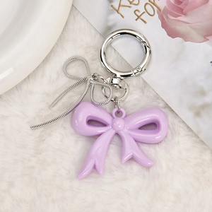 Detail of sweet purple resin bow keychain with silver butterfly charm on plush background