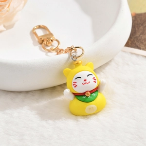 Macro shot of a yellow Maneki Neko lucky cat keychain with golden bell on a white tray