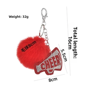 Macro shot of red pompom keychain with CHEER rhinestone trumpet charm on a white background