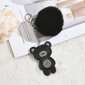 Detail of a black plush fur ball keychain with a rhinestone bear pendant and silver chain