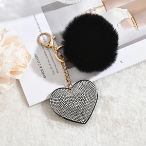 Macro detail of black faux fur pompom and sparkling rhinestone heart keychain on white fabric
