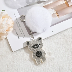 Sparkling rhinestone bear keychain with a fluffy white faux fur pompom on a magazine