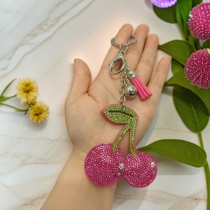 Detailed view of rhinestone cherry keychain with pink tassel and bell on palm
